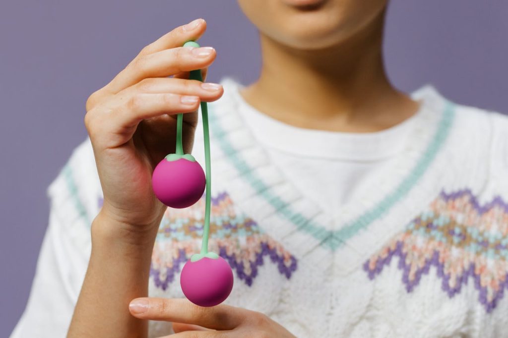 Detailed close-up of hands holding purple Kegel balls against a purple background.